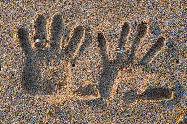 hands in the sand with wedding rings