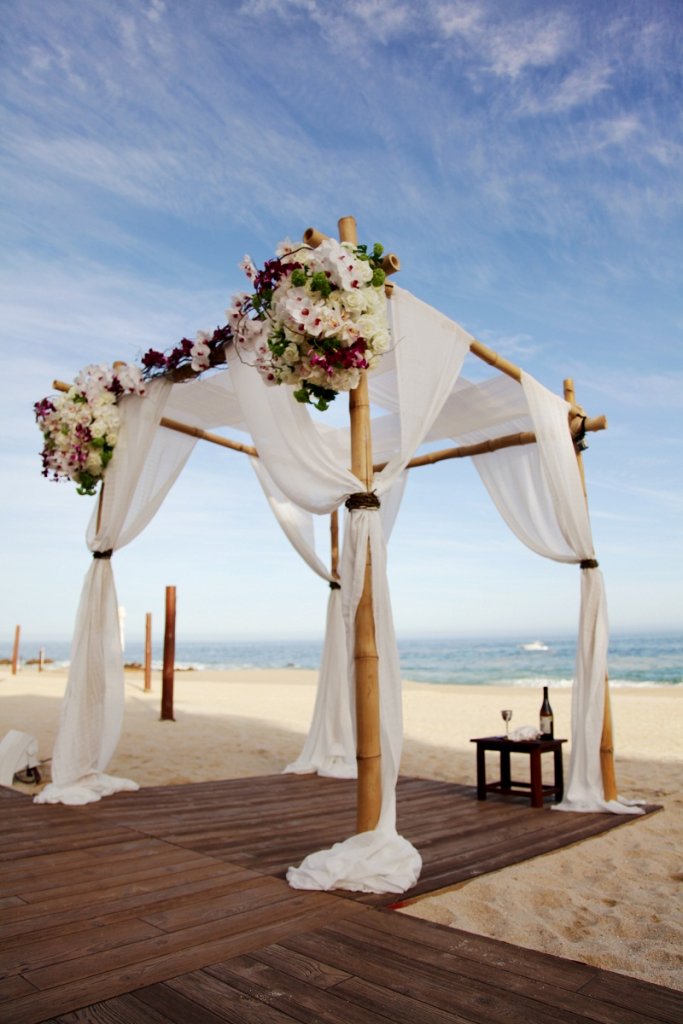 white draped arbor with wooden floors on the beach