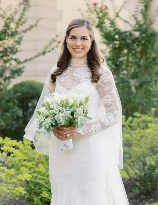Elegant bride holding a bouquet in a garden setting, wearing a lace wedding dress.