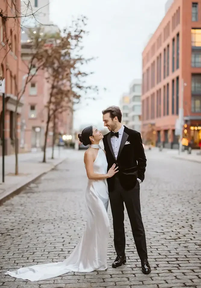 Elegant bride and groom in wedding attire on city street during daytime, romantic wedding scene.