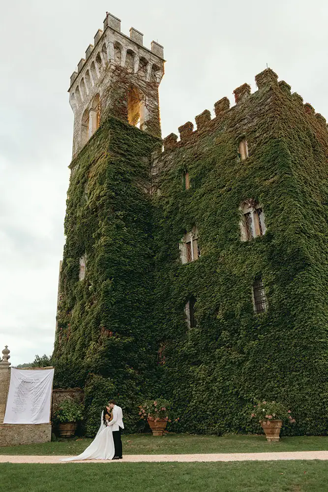 A lush, ivy-covered castle with a bride and groom in wedding attire standing in front.