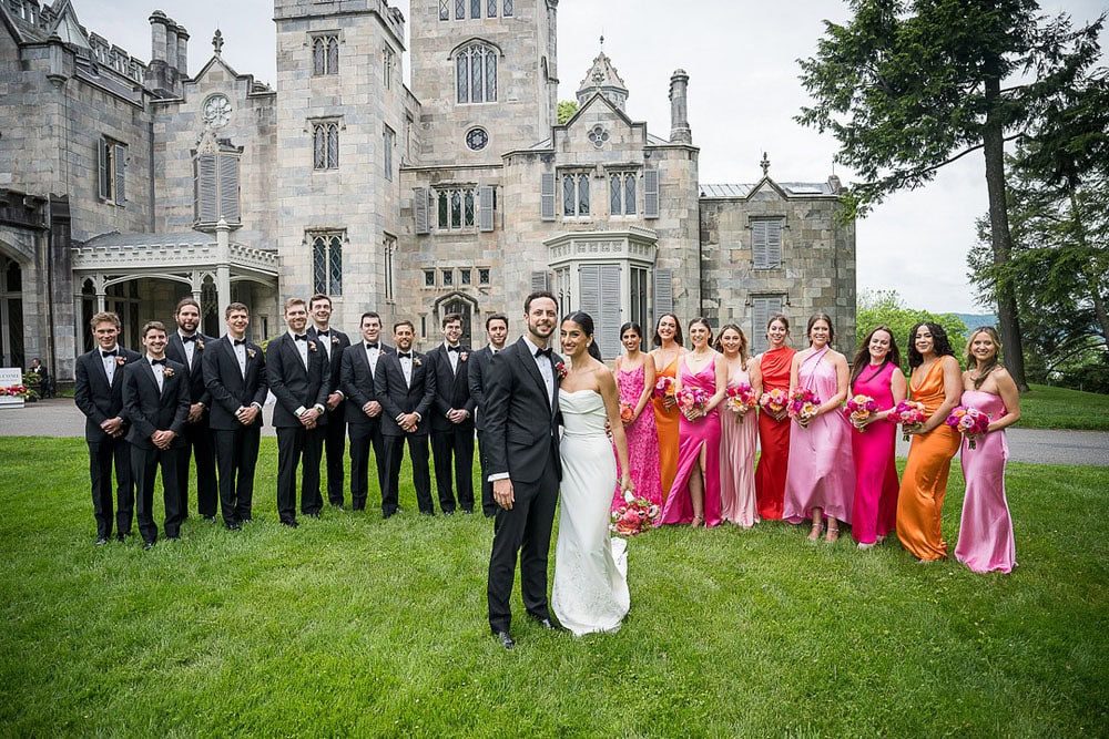 Elegant wedding party outside a historic castle with bride, groom, bridesmaids, and groomsmen.