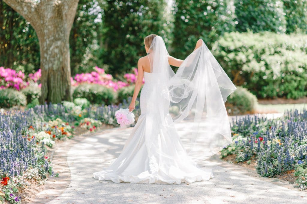 Elegant bride in a white wedding gown with veil in a garden setting.