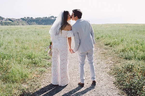 Romantic wedding couple holding hands outdoors in a green field.