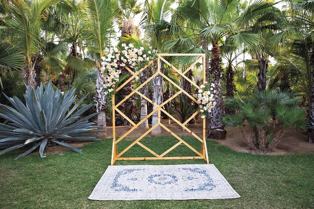 A lush outdoor wedding arch decorated with flowers in a tropical garden setting.