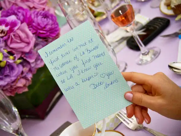 A heartfelt handwritten note on a wedding table setting with flowers and wine glasses.