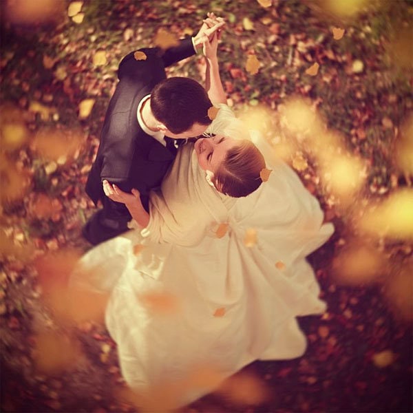 Romantic couple dancing in autumn leaves during wedding celebration.
