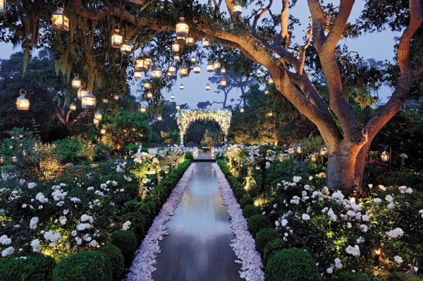 Elegant outdoor wedding aisle with hanging lanterns and floral decorations at dusk.