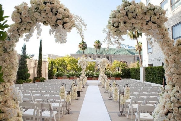 Elegant outdoor wedding ceremony setup with floral arches and white chairs.