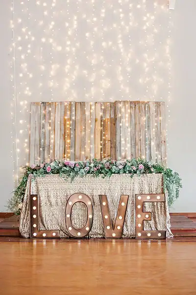 A romantic wedding decor setup with illuminated LOVE sign and fairy lights.