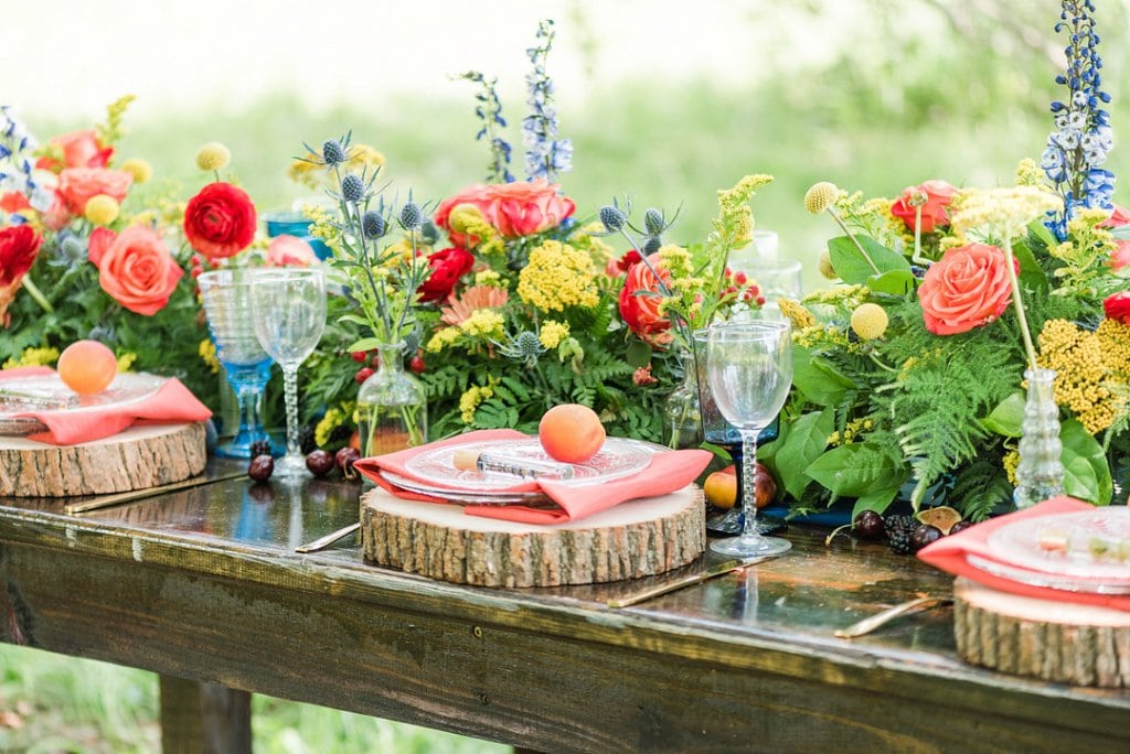 A colorful outdoor wedding table with floral centerpiece and rustic decor.