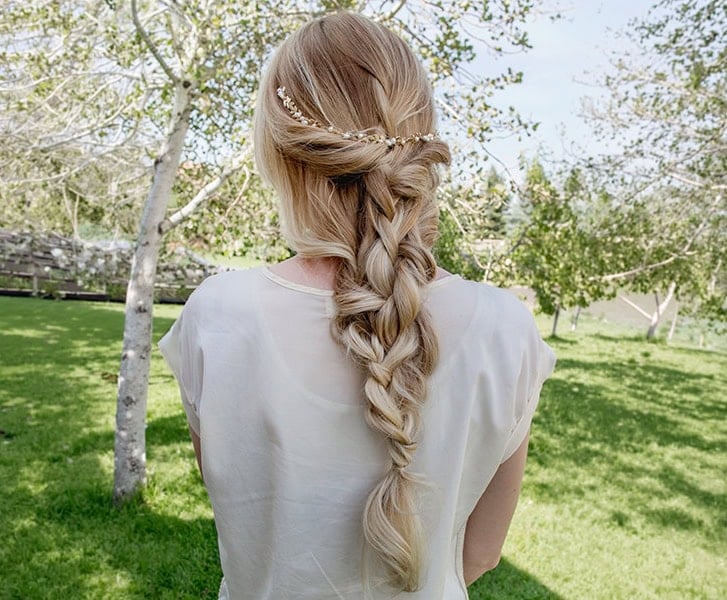 Bridal hairstyle with braid and floral hair accessory in outdoor garden setting.