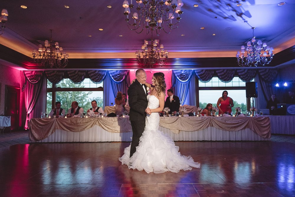 A wedding couple dancing in a decorated reception hall with pink and blue lighting.