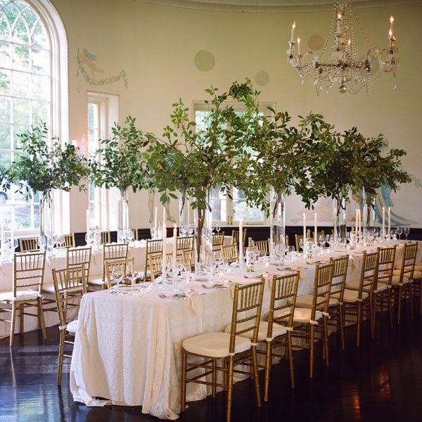 Elegant wedding reception table decorated with greenery and candles in a bright room.