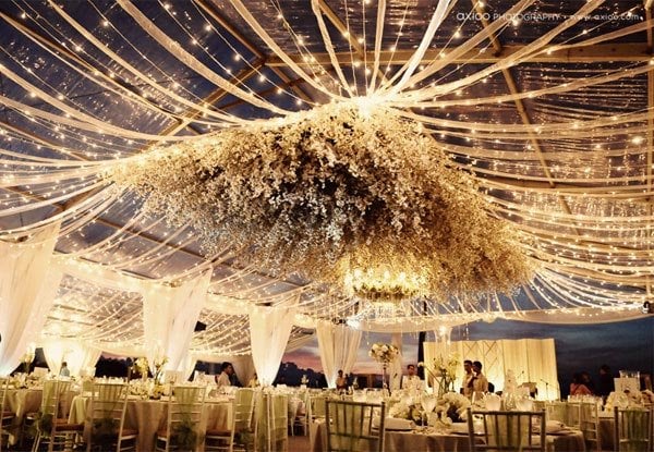 Elegant wedding reception with floral ceiling decor and string lights under a tent.
