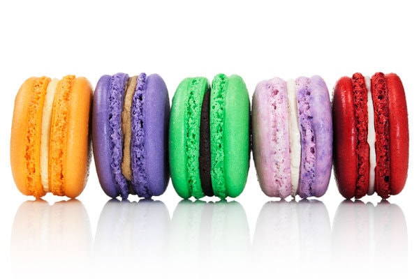 Bright colorful macarons in orange, purple, green, pink, and red on white background.