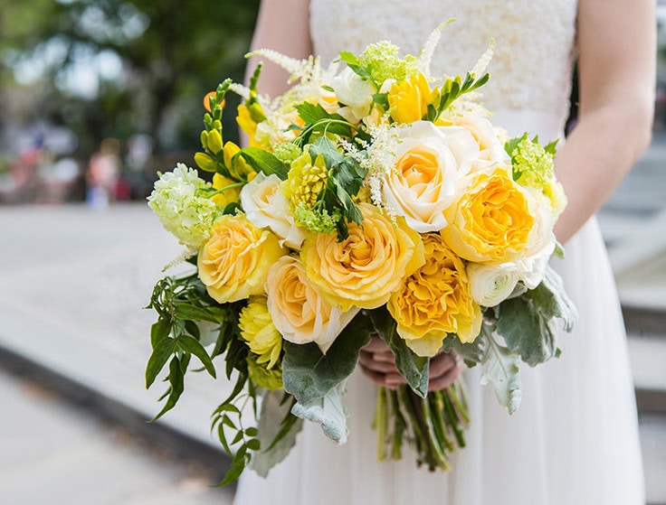 A bride holding a yellow and white floral bouquet outdoors on her wedding day.