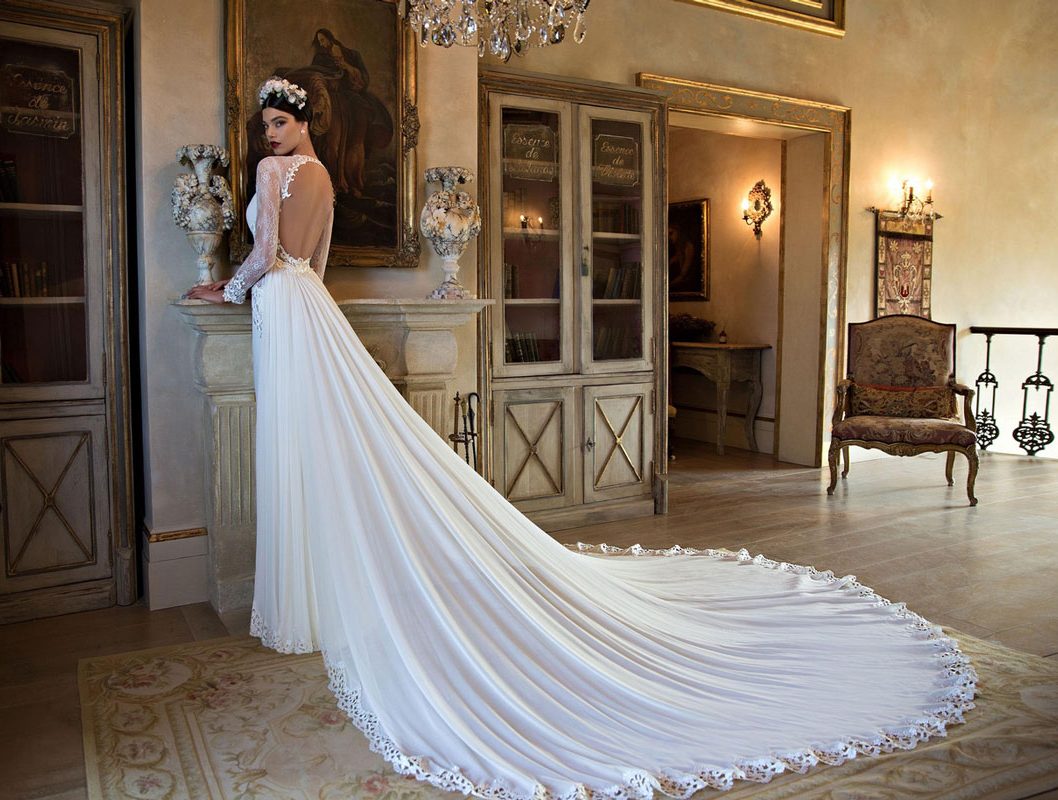 Elegant bride in a long white wedding gown with a train in a vintage-style room.