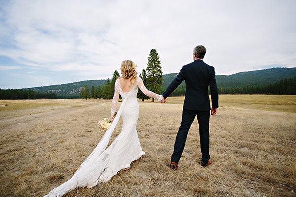 A lush outdoor wedding photo featuring a bride and groom holding hands in a scenic field.