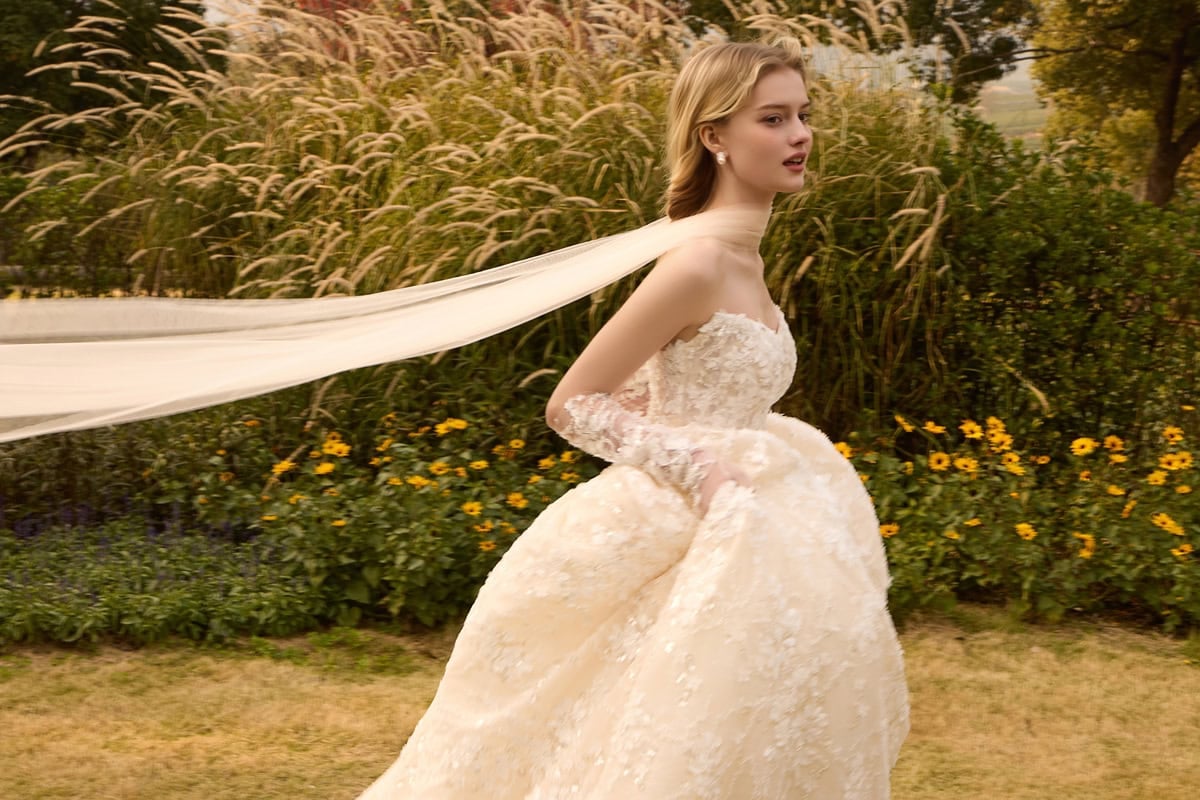 A bride in a lace wedding gown with a long veil outdoors in a garden setting.