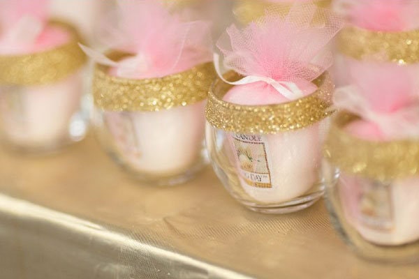 A romantic wedding favor with small glass jars decorated with pink tulle and gold glitter bands.