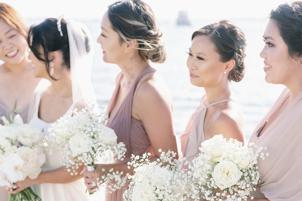 Elegant bridesmaids holding white bouquets at outdoor wedding reception.