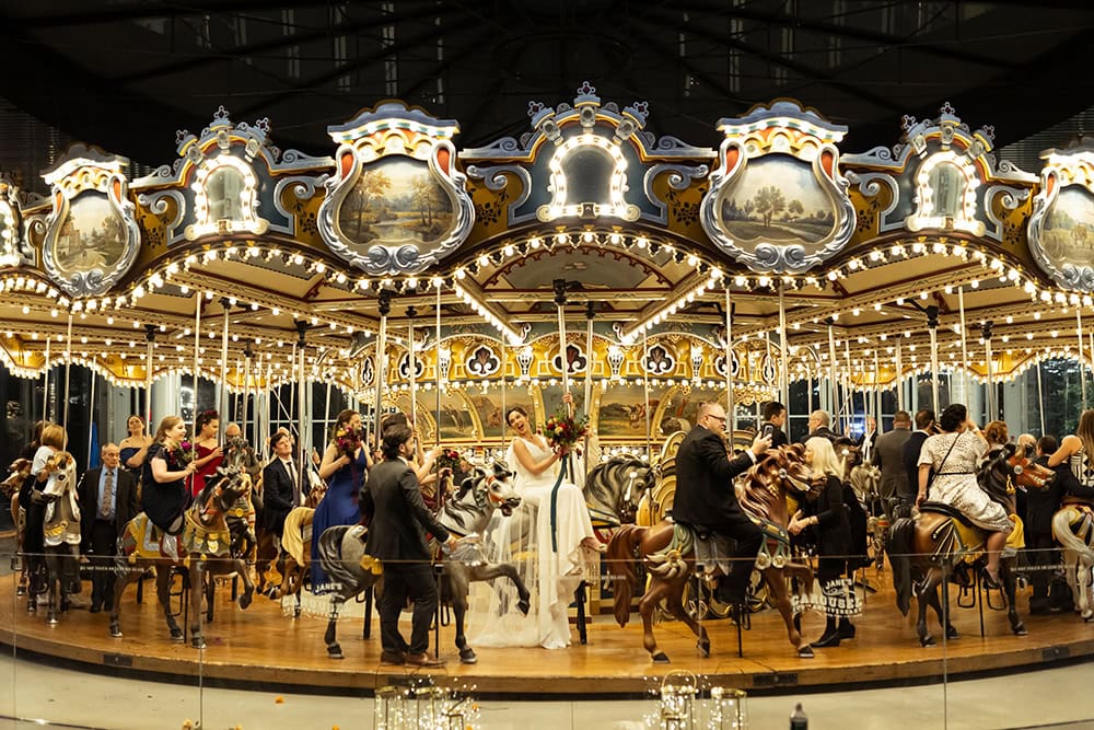 Elegant vintage carousel with couples and children enjoying a ride at a wedding celebration.