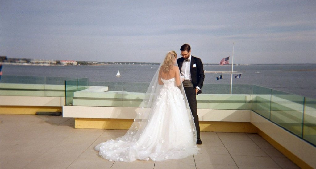 A bride and groom exchanging vows on a waterfront terrace with city skyline in the background.