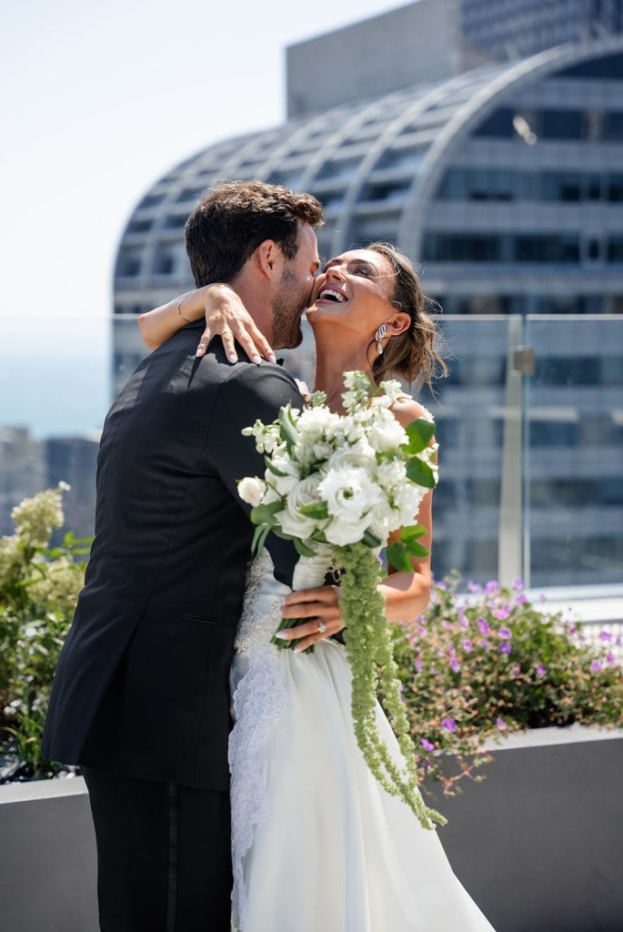 A couple celebrating their wedding outdoors with a modern cityscape background.
