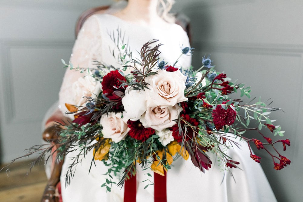 A lush bridal bouquet with roses, greenery, and deep red accents for wedding decor.