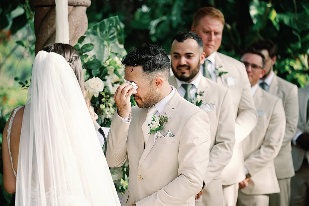 A wedding ceremony with groom emotional during vows in lush outdoor setting.