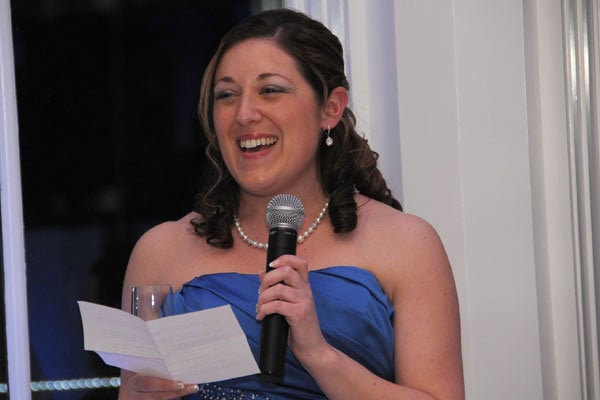 A woman in a blue dress giving a speech at a wedding reception.