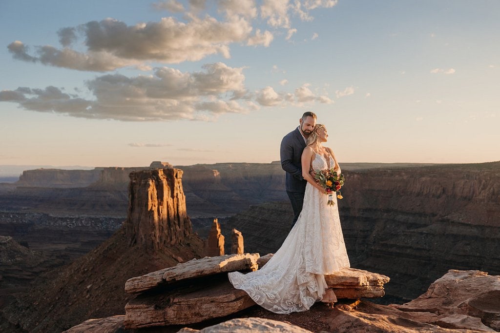 Romantic wedding couple on canyon edge at sunset with scenic views.