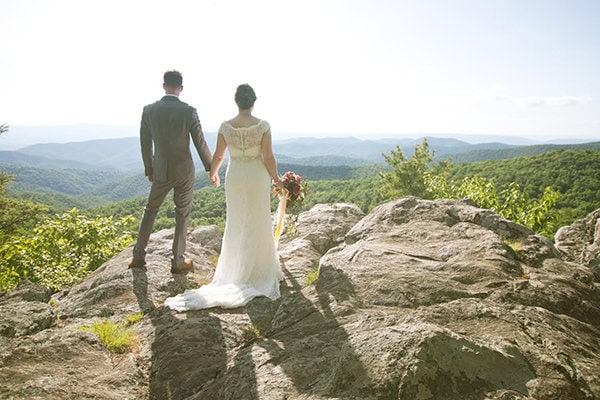 A couple in wedding attire holding hands on a rocky overlook with scenic mountain view in Shenandoah National Park.