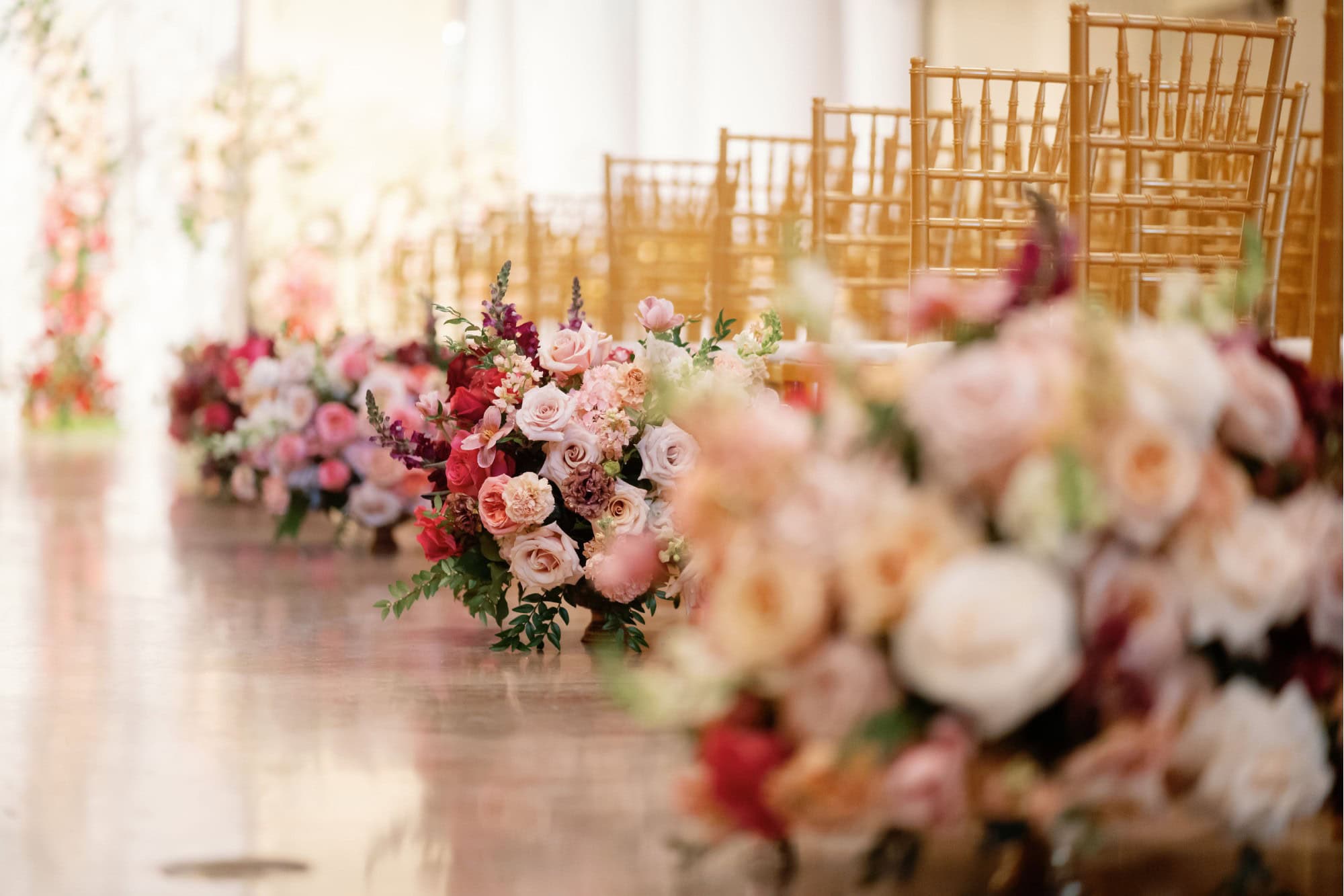 A beautiful floral wedding aisle with pink and white roses and gold chairs.
