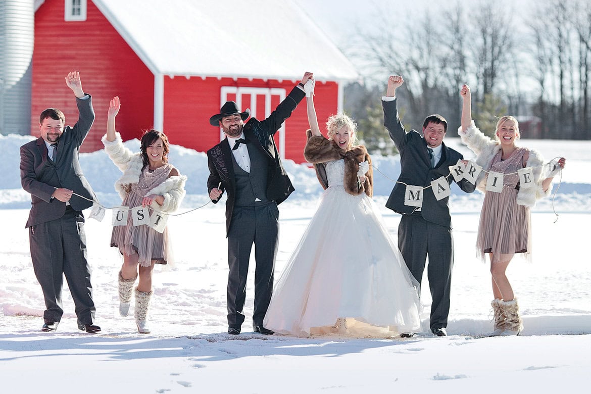 A joyful wedding celebration outdoors in winter with bride, groom, and friends holding "MARRY" and ".