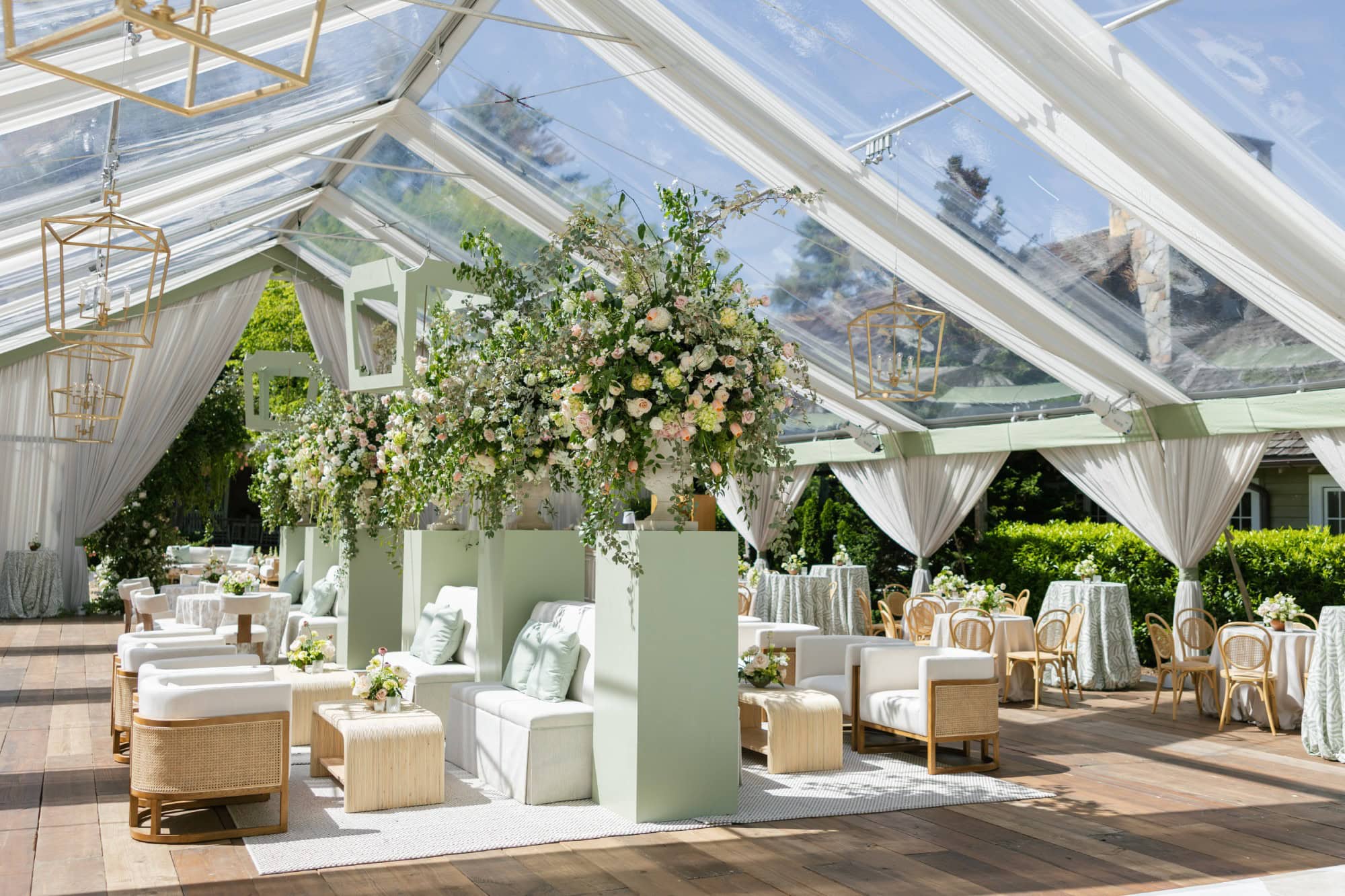 A lush floral centerpiece in a bright, elegant wedding reception tent with white drapery.
