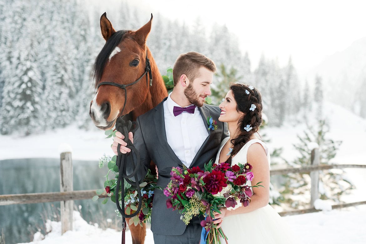 Romantic winter wedding with bride, groom, and horse in snowy landscape.