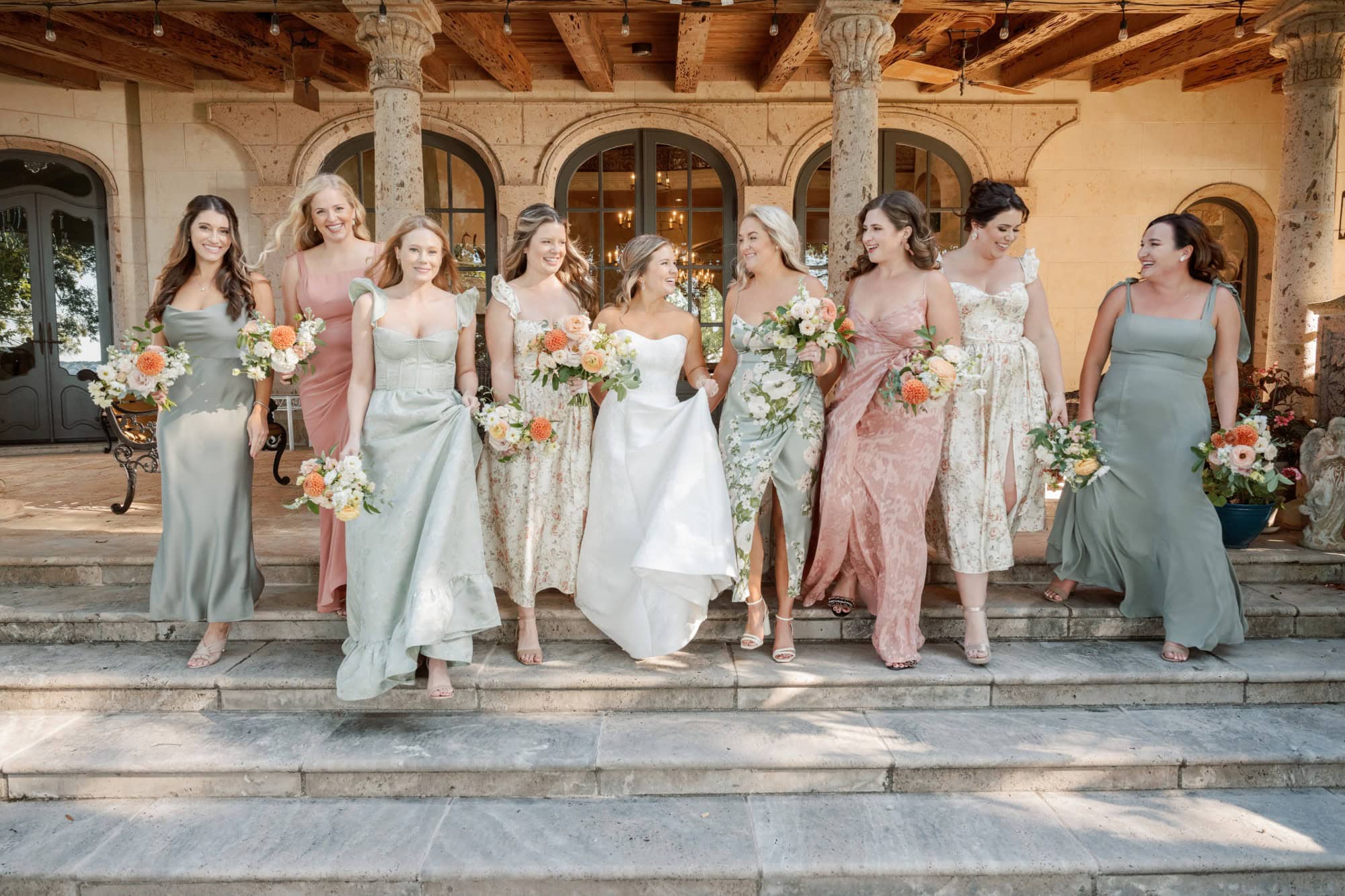 Elegant bridal party with bridesmaids in pastel dresses and bouquets on steps.