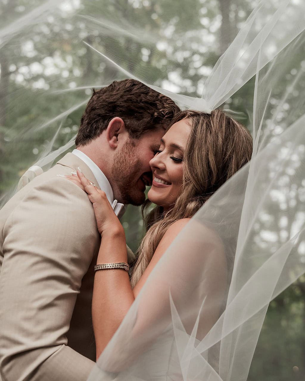 Bride and groom share a romantic moment under a sheer veil outdoors.