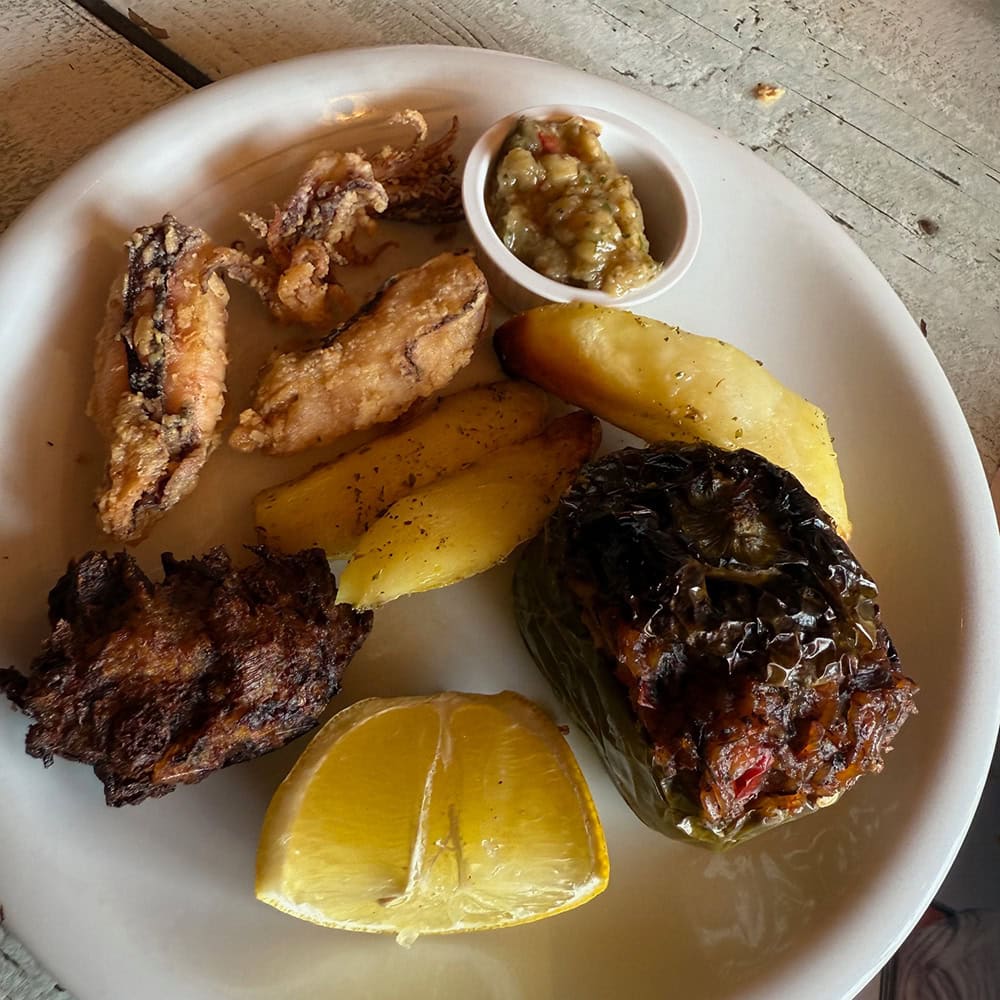 Fried fish, roasted vegetable, lemon wedge, and salsa on a white plate.