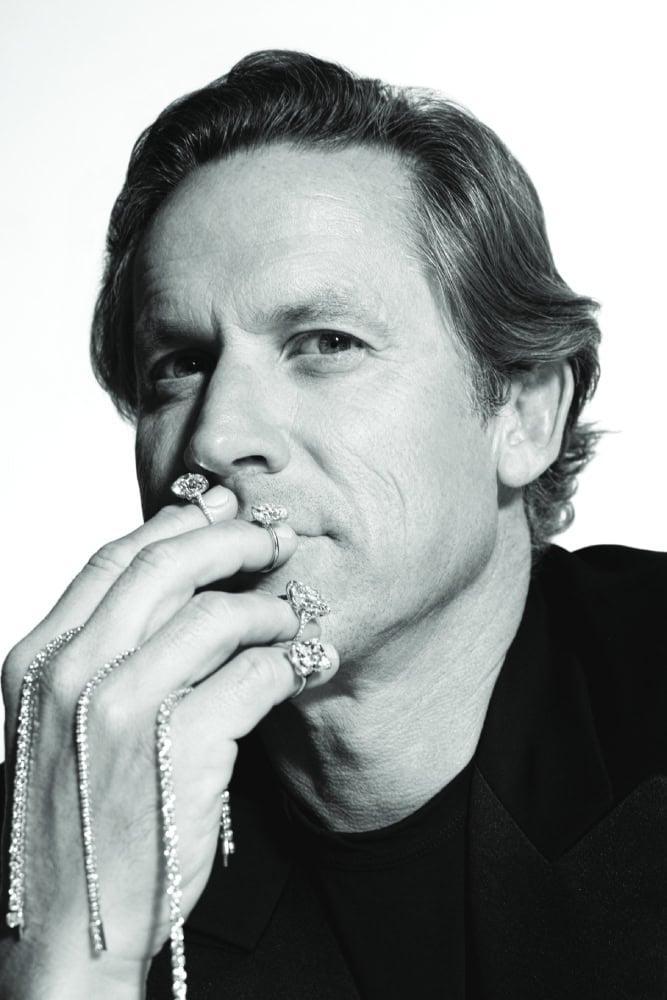 Black and white portrait of a man with styled hair, wearing rings and jewelry, looking contemplative.