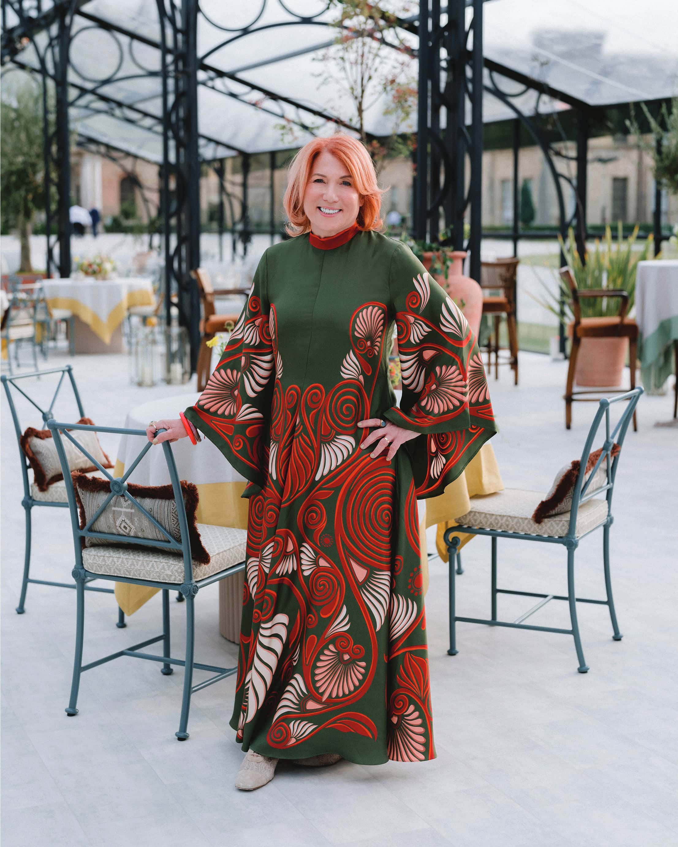 Woman in colorful patterned dress standing in outdoor dining area with tables and chairs.