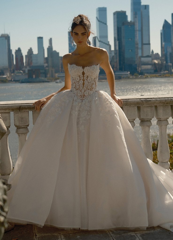 Bride in elegant wedding gown with city skyline in background.