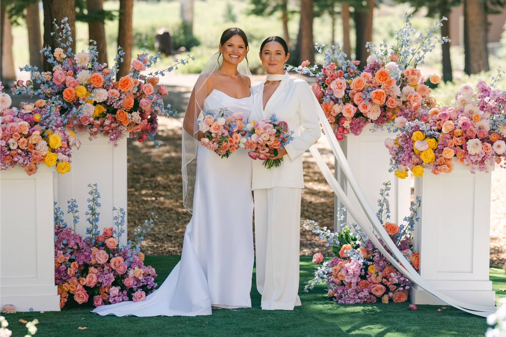 Elegant same-sex wedding ceremony with colorful floral arch and bouquets.