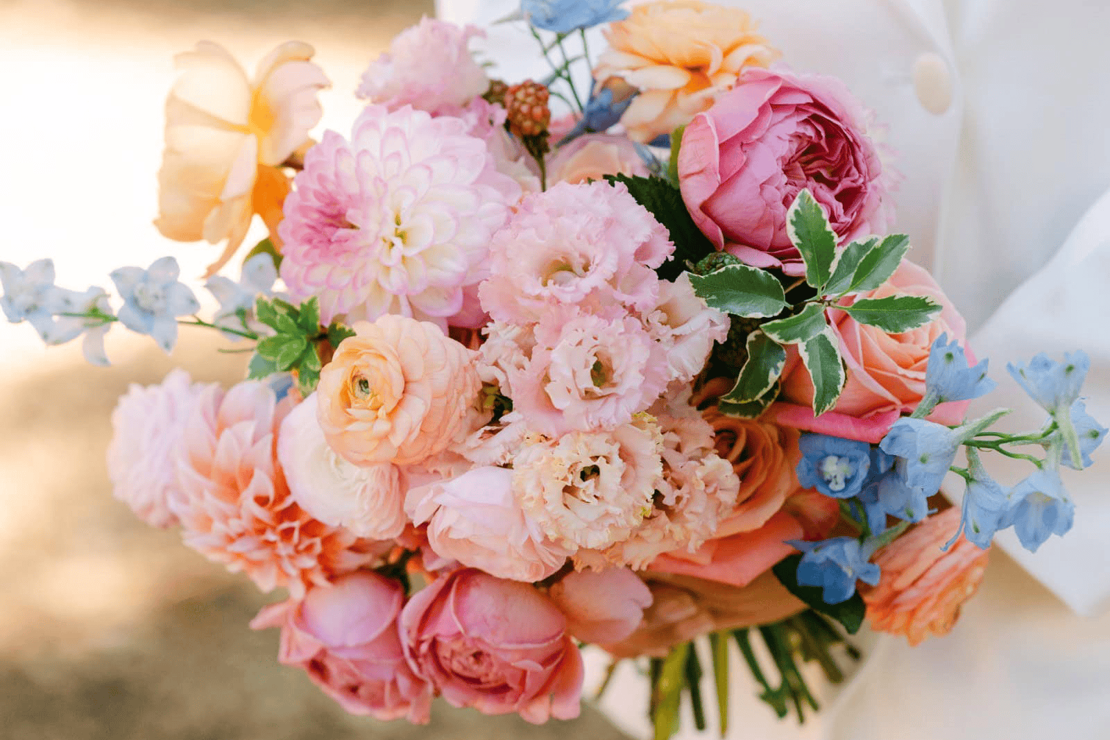 Beautiful pastel bridal bouquet with pink, peach, and blue flowers for wedding.