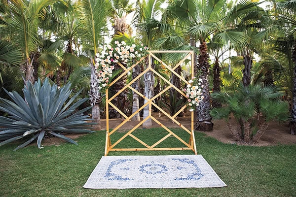 A lush outdoor wedding backdrop with floral arch and decorative rug in a tropical garden.