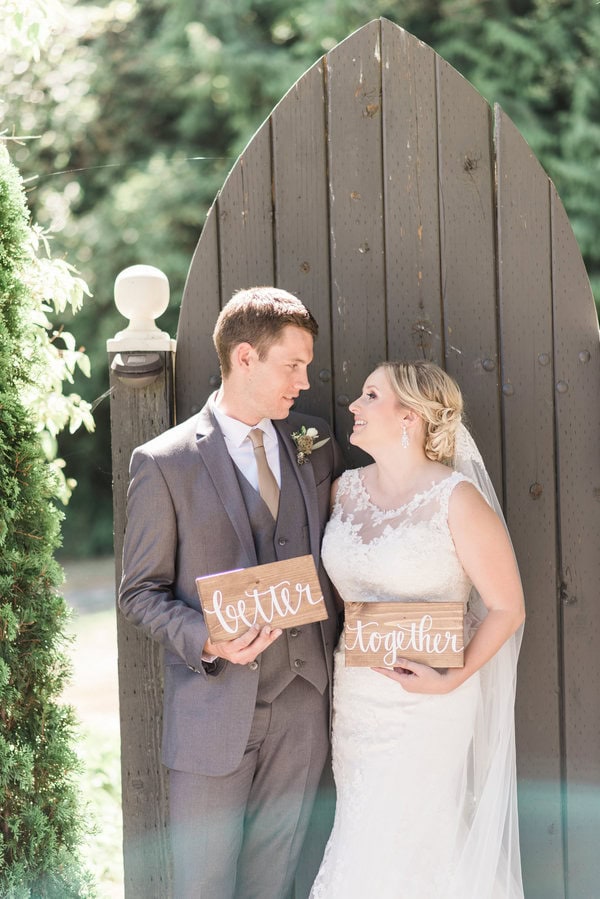 Bride and groom holding 'letter' and 'together' signs outside wedding venue.