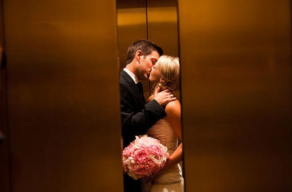 A couple sharing a romantic moment in an elevator with a bouquet of pink roses.
