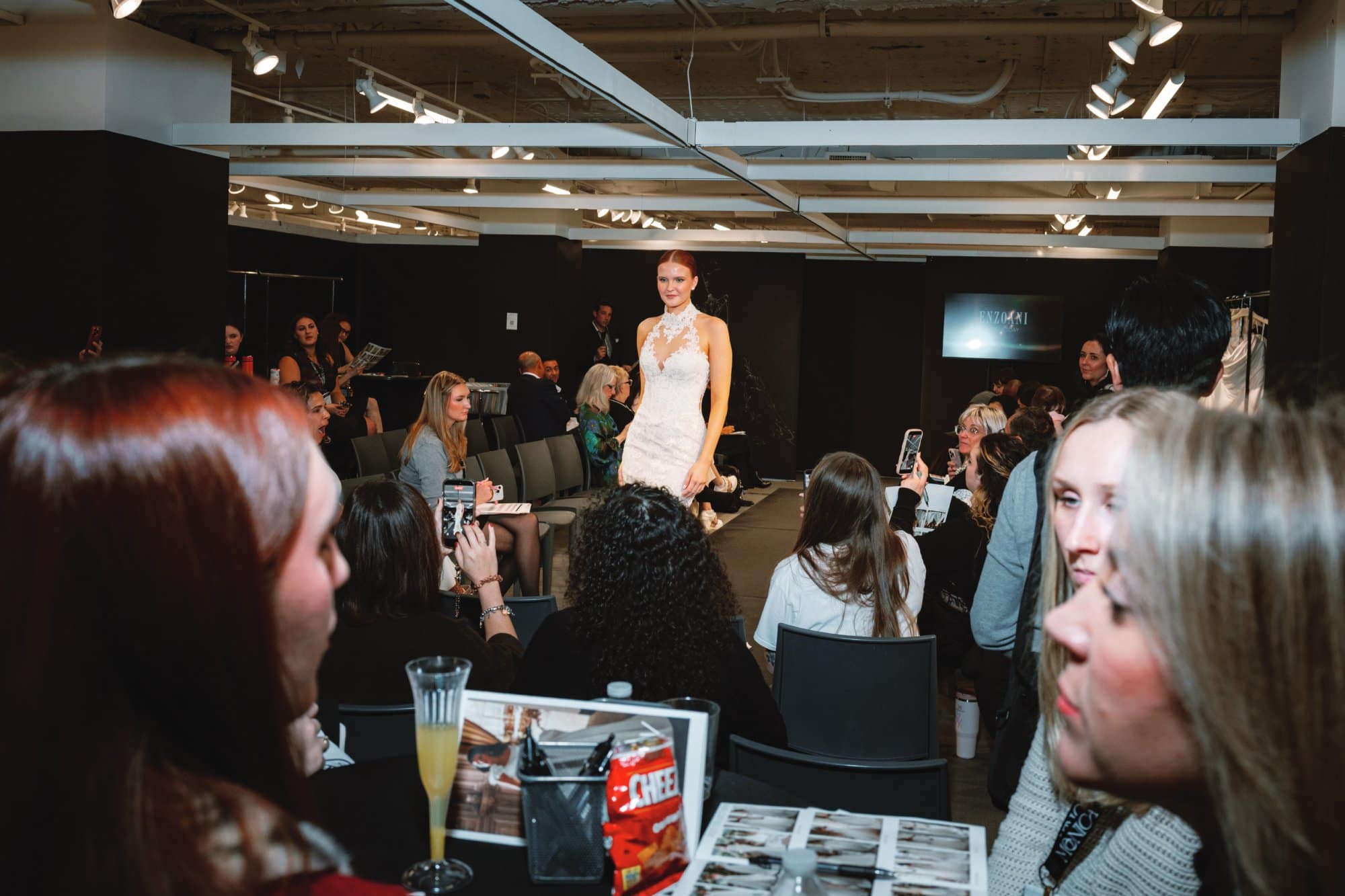 Model showcases wedding dress at bridal fashion event with audience watching.